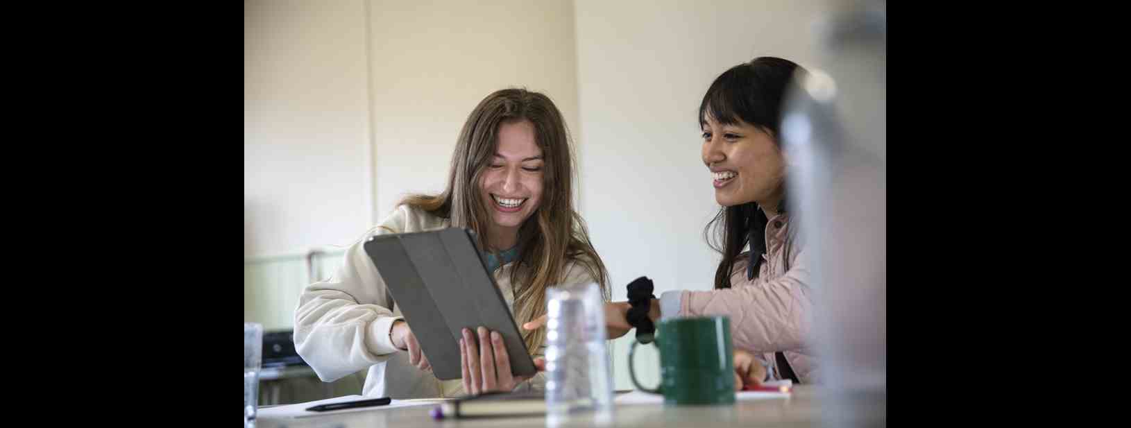 Two further education students sat smiling at an iPad.